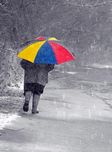 Person in heavy coat and bright umbrella walking in snow storm.